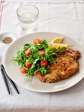 Delicious crispy chicken milanese plated alongside a vibrant tomato and arugula salad. Freshly squeezed lemon adds a zesty touch to this healthy dish, perfect for lunch or dinner