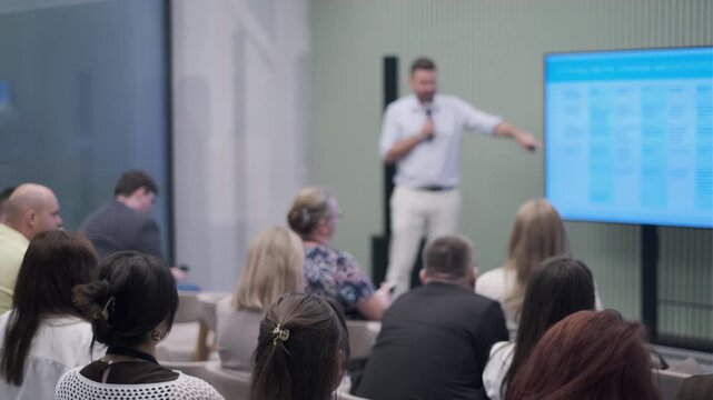 Audience attentively listens to a speaker giving a presentation during a business conference.
