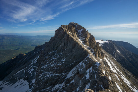 Aerial view of the jagged peaks of Mount Olympus reach towards the sky, where the blue fades into a soft horizon, Litochoro, Olimpos, Greece.