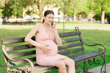 pregnant woman sits on a park bench and talking on phone