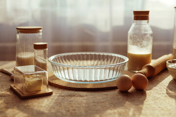 
Ingredients for baking a pie: a glass pie dish, a stick of butter, two eggs, and various dry ingredients in glass containers on a rustic cloth.