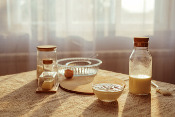 A sunny kitchen counter displays baking ingredients, including a glass bowl of batter, milk in a...