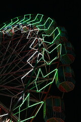 A brightly illuminated ferris wheel with colorful neon lights creating intricate patterns in the night, showcasing a vibrant atmosphere often found in amusement parks or festive celebrations.