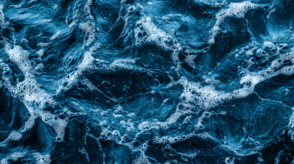A close-up view of dark blue ocean water with swirling patterns and bubbles, creating a dynamic and textured surface.