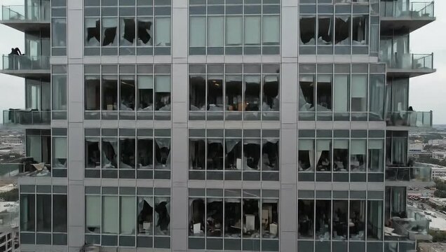 Gray facade of a modern office building with shattered windows and torn curtains hanging out