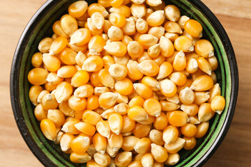 Yellow popcorn kernels in bowl closeup. Raw dried maize seeds in black ceramic dish on wooden...