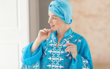 Bride is looking out the window waiting for the groom. Woman in blue colored clothes and turban of the east asian type.