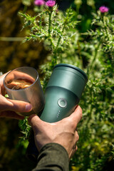 Hands holding a portable coffee maker and cup with fresh espresso in morning light