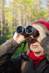 A middle-aged girl in a red hat and a green jacket stands in the forest on a sunny day and looks...