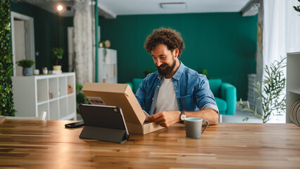 Happy freelancer unboxing parcel at home office desk