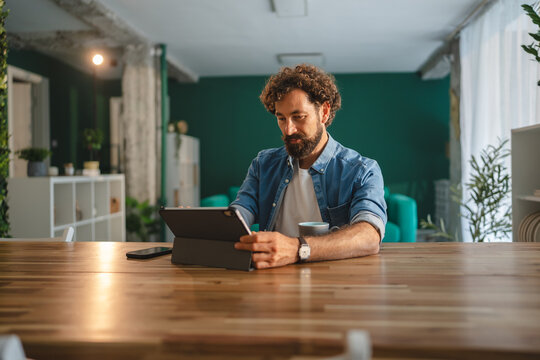 Focused freelancer working from home using digital tablet and drinking coffee