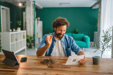 Man managing home finances holding coin and checking invoice