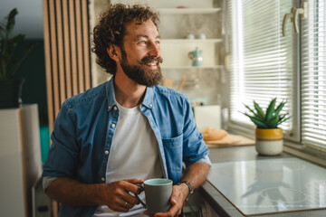 Smiling man drinking coffee and looking out the window in kitchen