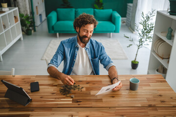 Smiling freelancer counting coins and reviewing invoices at home office desk