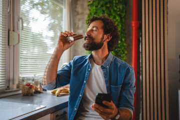 Man drinking protein shake and using smart phone in kitchen