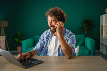 Smiling freelancer talking on phone and working on laptop at home