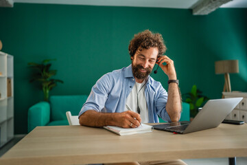 Freelancer smiling and taking notes during a video call from home office