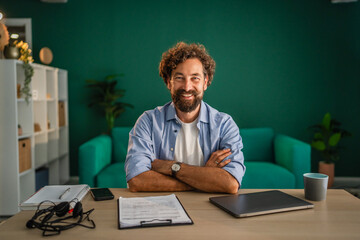 Confident entrepreneur smiling with crossed arms in home office