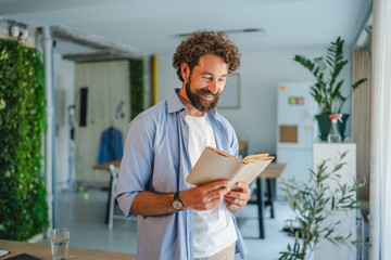 Smiling freelancer reading a book in his modern office