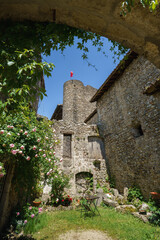Charming courtyard with wildflowers and rustic furniture beneath a medieval watchtower and stone ramparts of Pérouges, France; concept: heritage, rural charm.
