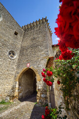 Medieval city gate and stone walls of Pérouges, France, viewed from a low angle with vibrant red roses in the foreground; concept: heritage, romance, historic travel.