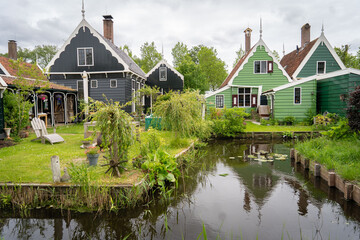 Dutch typical landscape. Traditional old dutch windmill with old houses against blue cloudy sky in the Zaanse Schans village, Netherlands. Famous tourism place. Sheep grazing on green grass.