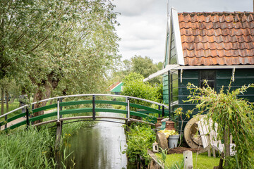 Dutch typical landscape. Traditional old dutch windmill with old houses against blue cloudy sky in the Zaanse Schans village, Netherlands. Famous tourism place. Sheep grazing on green grass.
