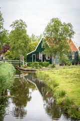Dutch typical landscape. Traditional old dutch windmill with old houses against blue cloudy sky in the Zaanse Schans village, Netherlands. Famous tourism place. Sheep grazing on green grass.