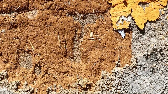 Slow horizontal panning video of an old weathered wall with peeling yellow paint, exposed adobe texture, and coarse cement. Ideal for use as a background or overlay in architectural or design pro