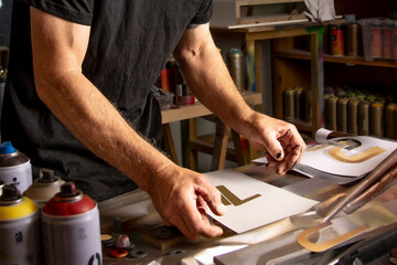 Close-up of an artist arranging letter stencils in a spray paint studio, capturing the raw creativity and precision of urban street art in action.