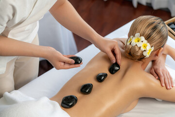 Hot stone massage at spa salon in luxury resort with day light serenity ambient, blissful woman...