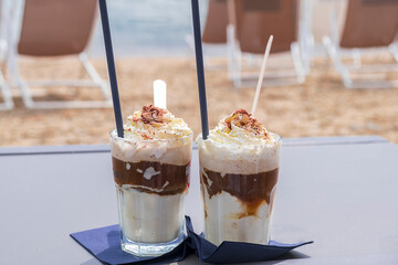 Two glasses of iced coffee with cream and chocolate on the beach.