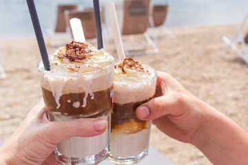 Male and female hands holding a glass of iced coffee at the beach.