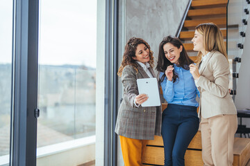 Group of Three Female Colleagues Smiling and Sharing Ideas Using a Digital Tablet