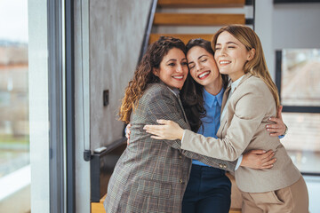 Three Female Colleagues Sharing a Warm Group Hug in a Modern Workplace