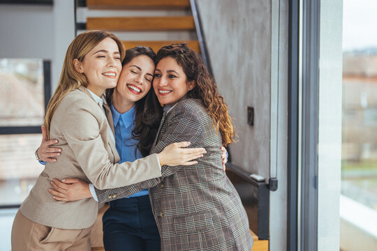 Three Professional Women Hugging and Smiling in a Modern Office Environment