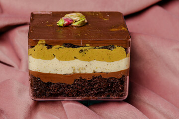 Layered dessert in a clear container, topped with pistachio. The dessert is layered with dark chocolate, cream and a pistachio-flavored mousse.