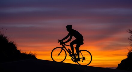 Silhouette of cyclist riding bicycle against colorful sunset sky on a hill at dusk or dawn time