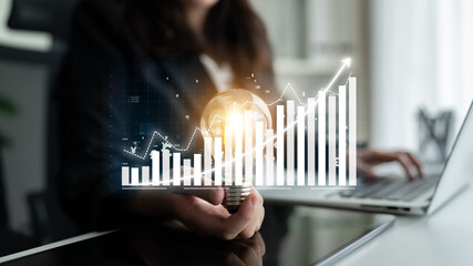 A business professional holds a light bulb representing innovation while analyzing growth charts on a laptop, illustrating progress and creative thinking in the workplace. Impute