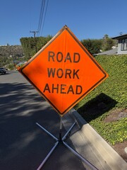 Road Work Ahead Sign: Bright orange road sign warning of upcoming construction zone on public street