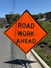 Road Work Ahead Sign: Bright orange road sign warning of upcoming construction zone on public street