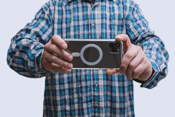 Close-up of a man in a plaid shirt taking a photo with a modern smartphone in landscape mode. Mobile photography, tech usage and content creation.