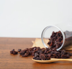 Raisins in wooden spoon on wooden table background.  Raisins spilling out of jar. Dry raisins. Selective focus.