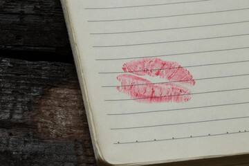 An open notebook with lines lies on a wooden table, at the bottom of the page there is a clear kiss...
