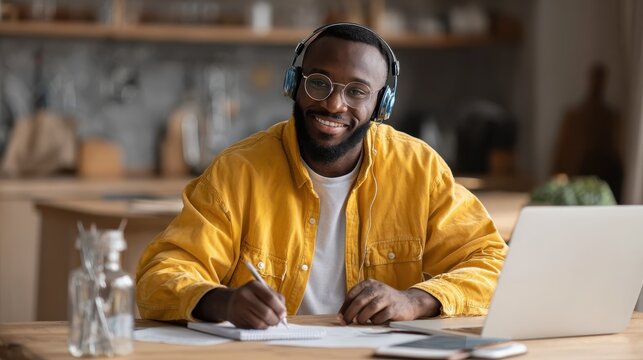Young happy smiling African American adult student wearing headphones having virtual education class meeting online call e learning webinar on laptop at home office writing notes., no logos, no brand
