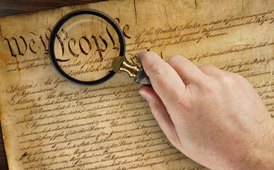 Male Hand Holding Magnifying Glass Over The Work People on the United States Constitution.