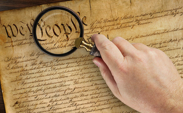 Male Hand Holding Magnifying Glass Over The Work People on the United States Constitution.