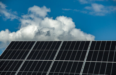 Solar panels under a bright blue sky with white clouds. Clean and renewable energy concept with a...