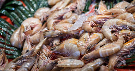 Close-up of fresh raw shrimp displayed on green leaves with ice, showcasing seafood freshness and texture at a local fish market or seafood stall.