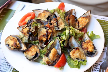 Delicious baked mussels served on a fresh salad on  outdoor french cafe table